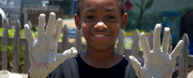 Young boy displays clay covered hands.