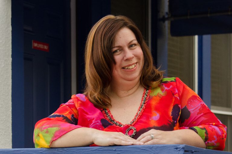 Smiling woman in red top poses in front of women's shelter.