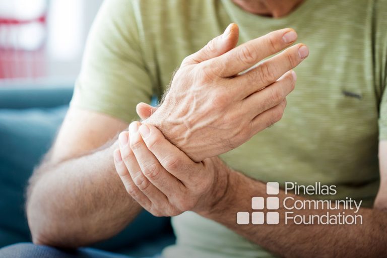 Elderly man rubs aching wrist while discussing pain management options with doctor.
