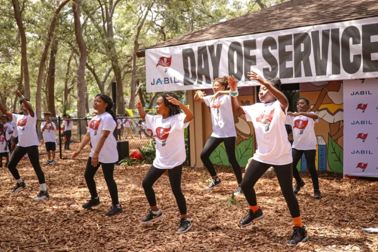 Young Artz 4 Life dancers perform outdoors in front of a Day of Service banner.