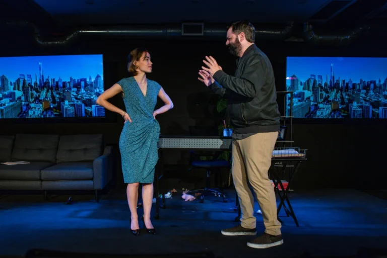 Two actors perform a scene on stage at The Studio@620, with city skyline projections behind them.